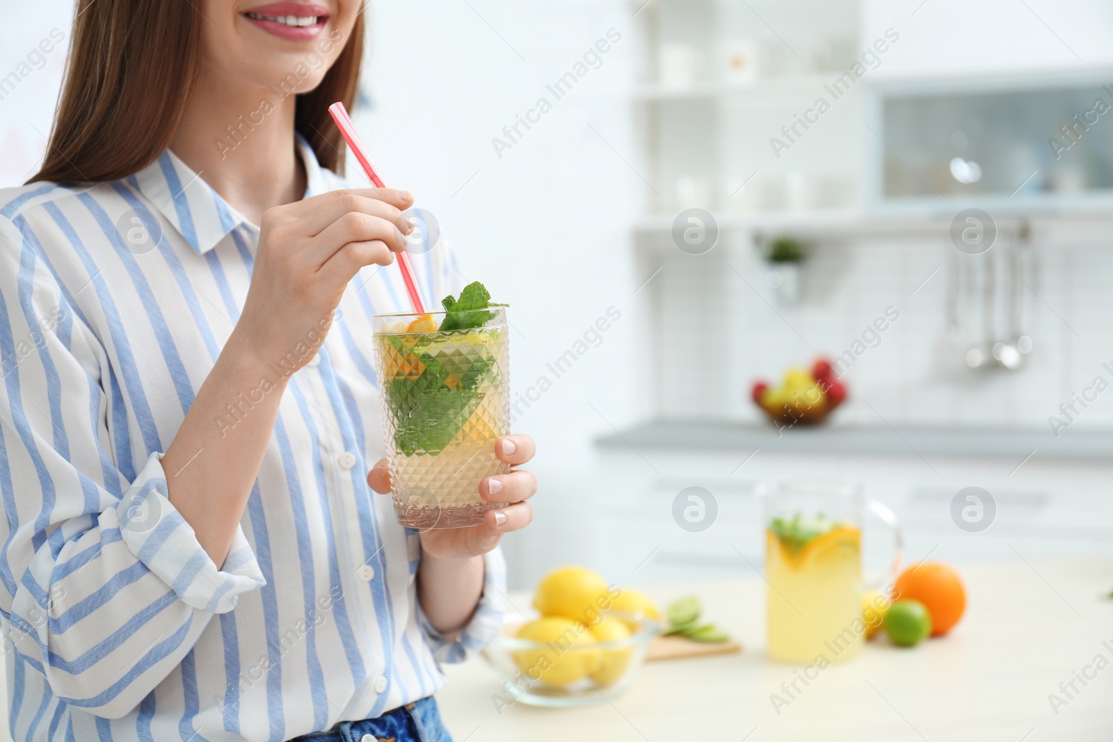 Photo of Woman with glass of natural detox lemonade in kitchen, closeup. Space for text