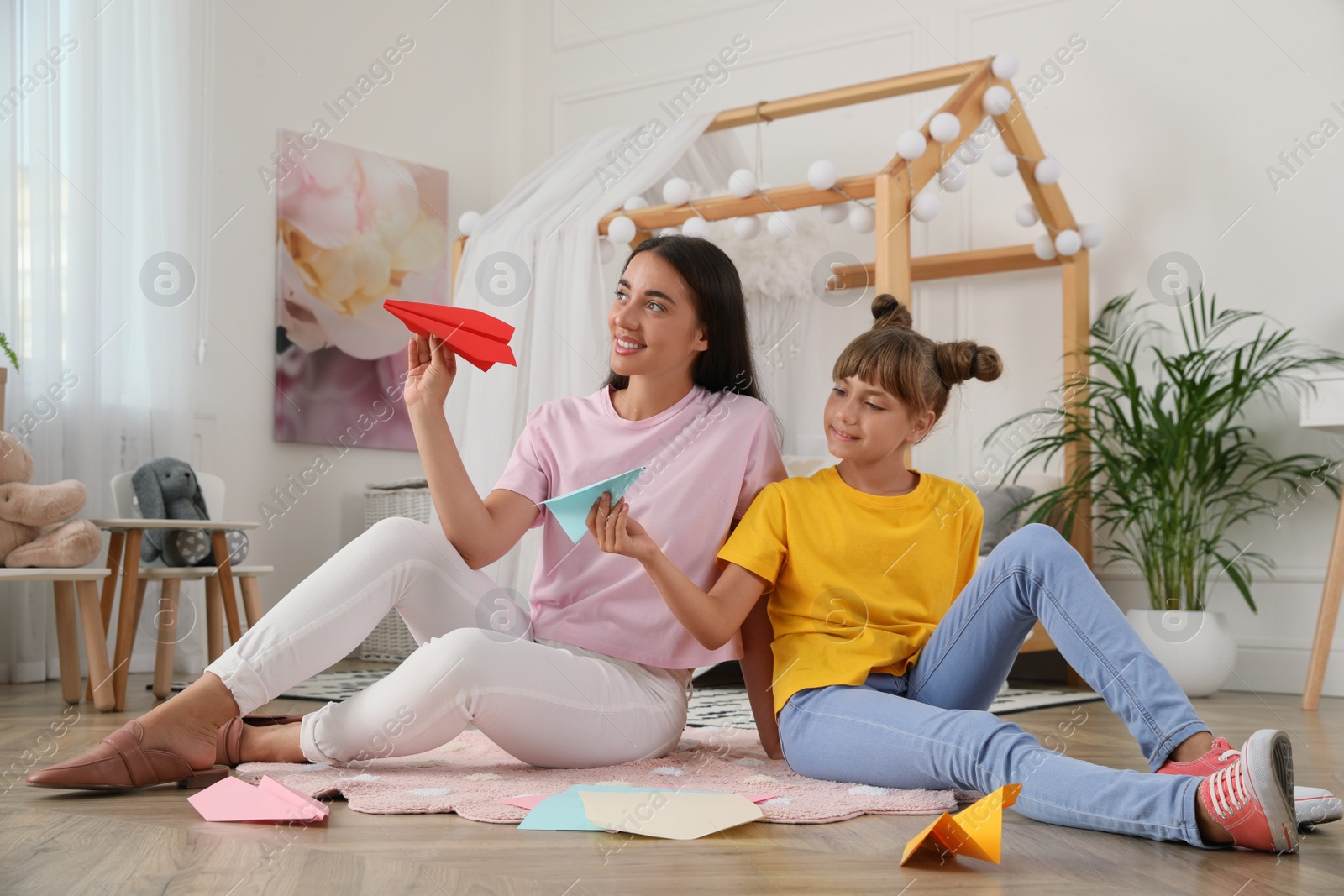 Photo of Happy mother and daughter playing with paper planes on floor in room