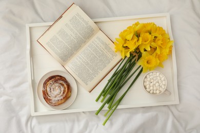 Bouquet of beautiful daffodils, bun and coffee on bed, top view