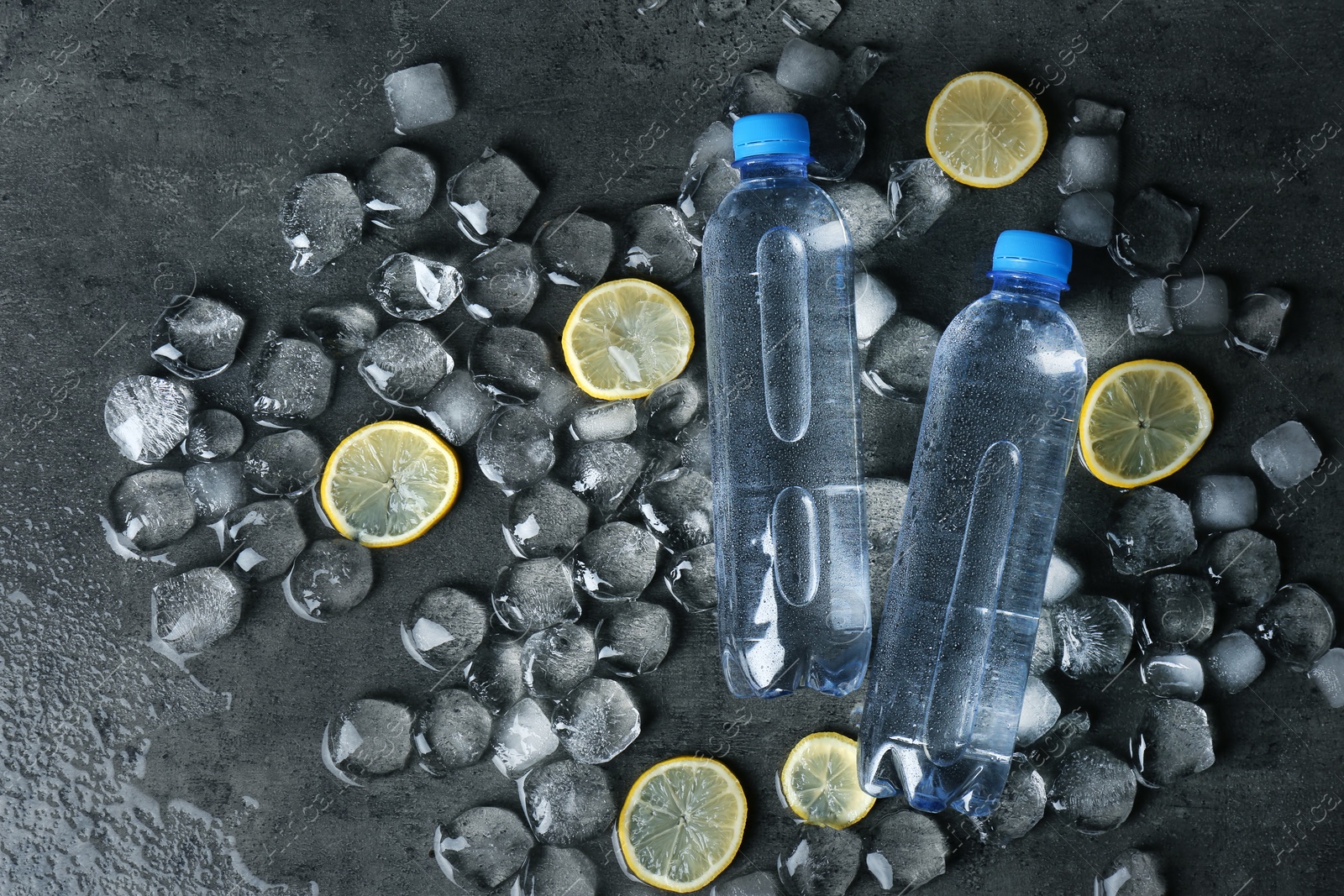 Photo of Flat lay composition with bottles of water, lemon slices and ice cubes on dark background