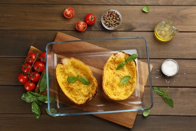 Photo of Halves of cooked spaghetti squash in baking dish and ingredients on wooden table, flat lay