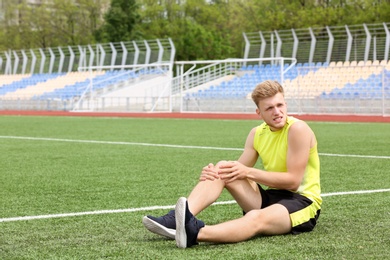 Man in sportswear suffering from knee pain at soccer field