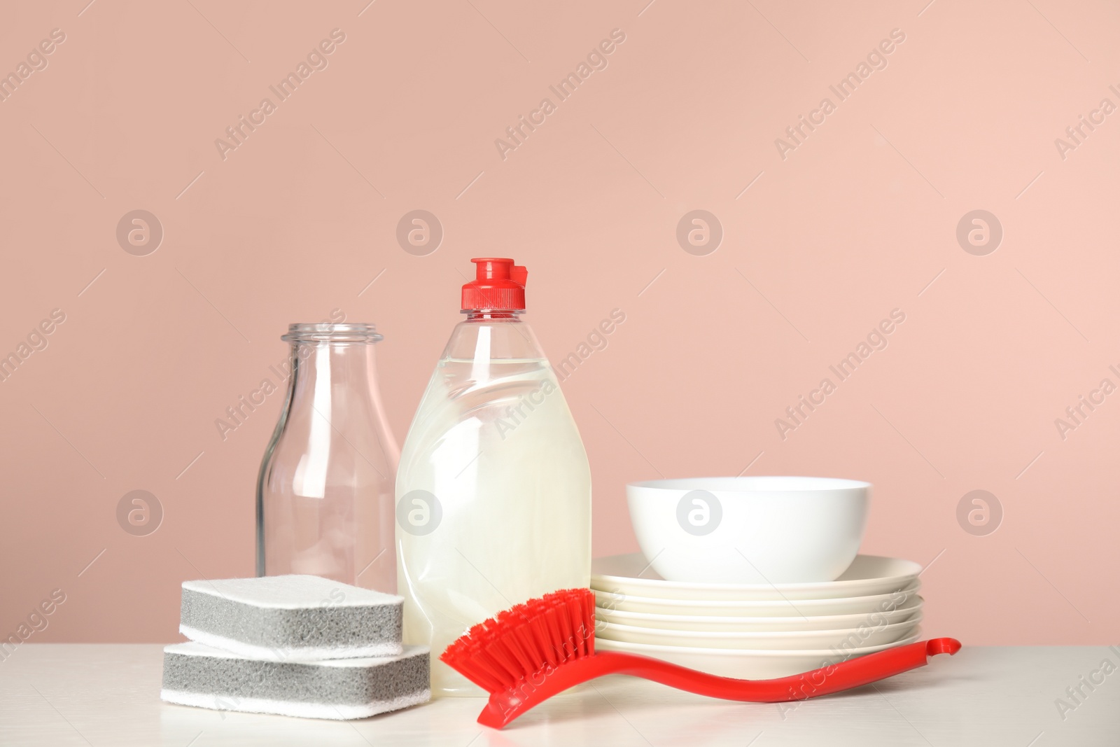 Photo of Cleaning supplies for dish washing and plates on white table against pink background