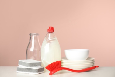 Photo of Cleaning supplies for dish washing and plates on white table against pink background