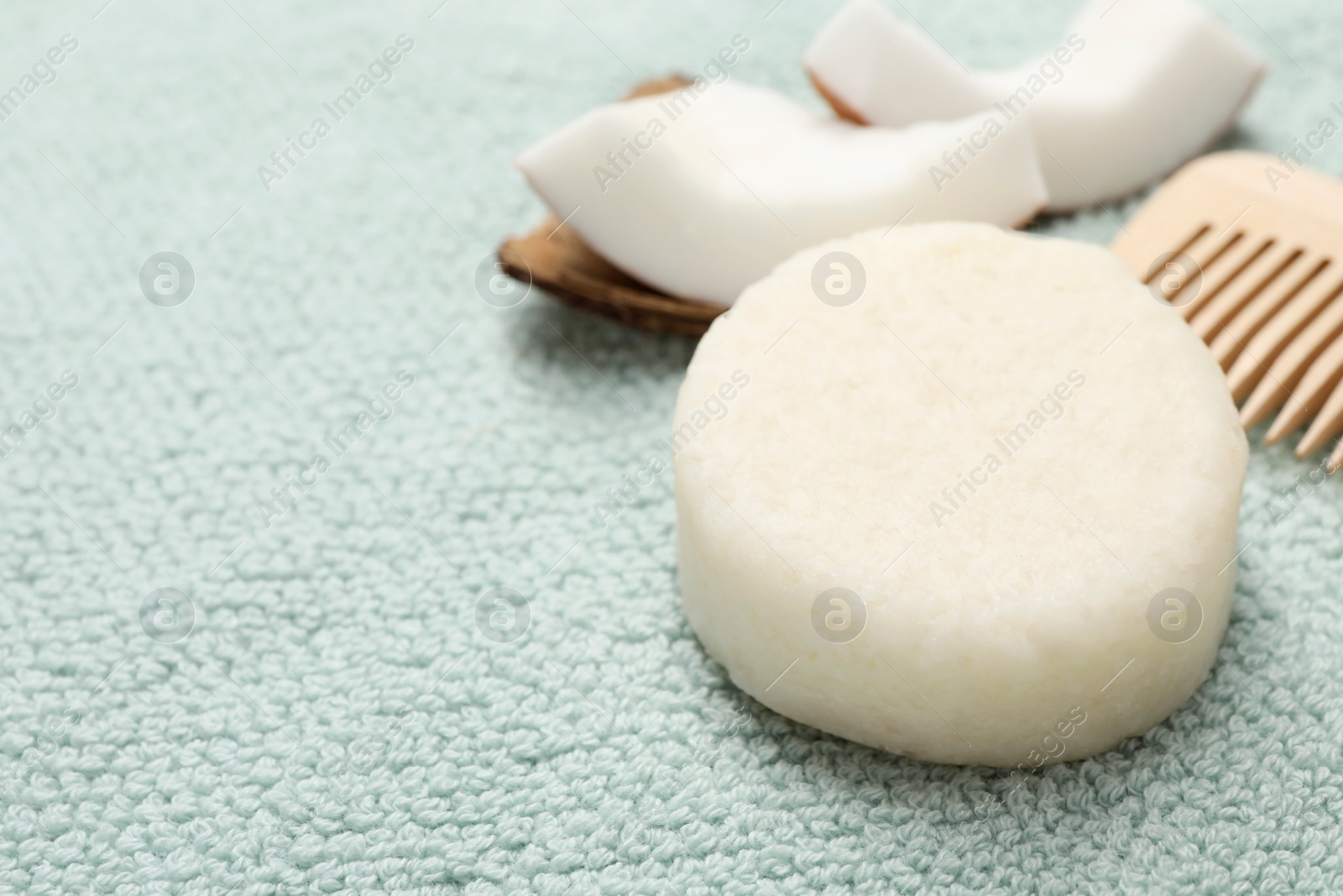 Photo of Solid shampoo bar, comb and coconut on light blue cloth, closeup. Space for text