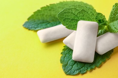 Tasty white chewing gums and mint leaves on yellow background, closeup. Space for text