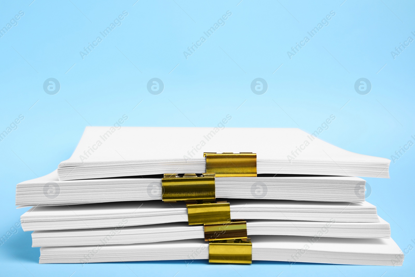 Photo of Many sheets of paper with golden clips on light blue background, closeup