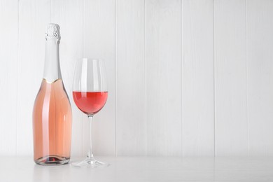 Photo of Bottle and glass of delicious rose wine on table against white wooden background. Space for text