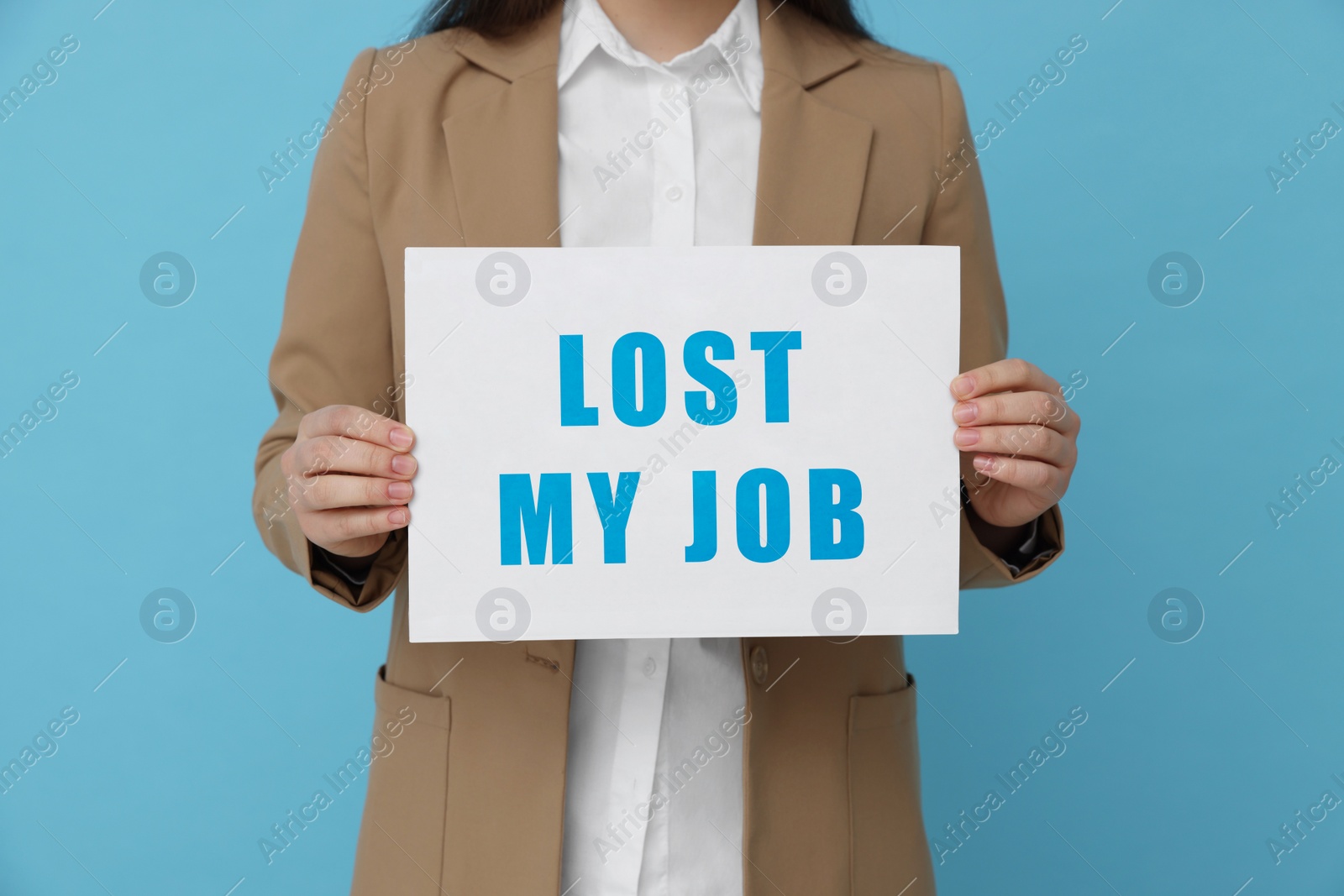 Image of Unemployed woman holding sign with phrase Lost My Job on light blue background, closeup