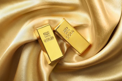 Photo of Gold bars on shiny silk fabric, flat lay