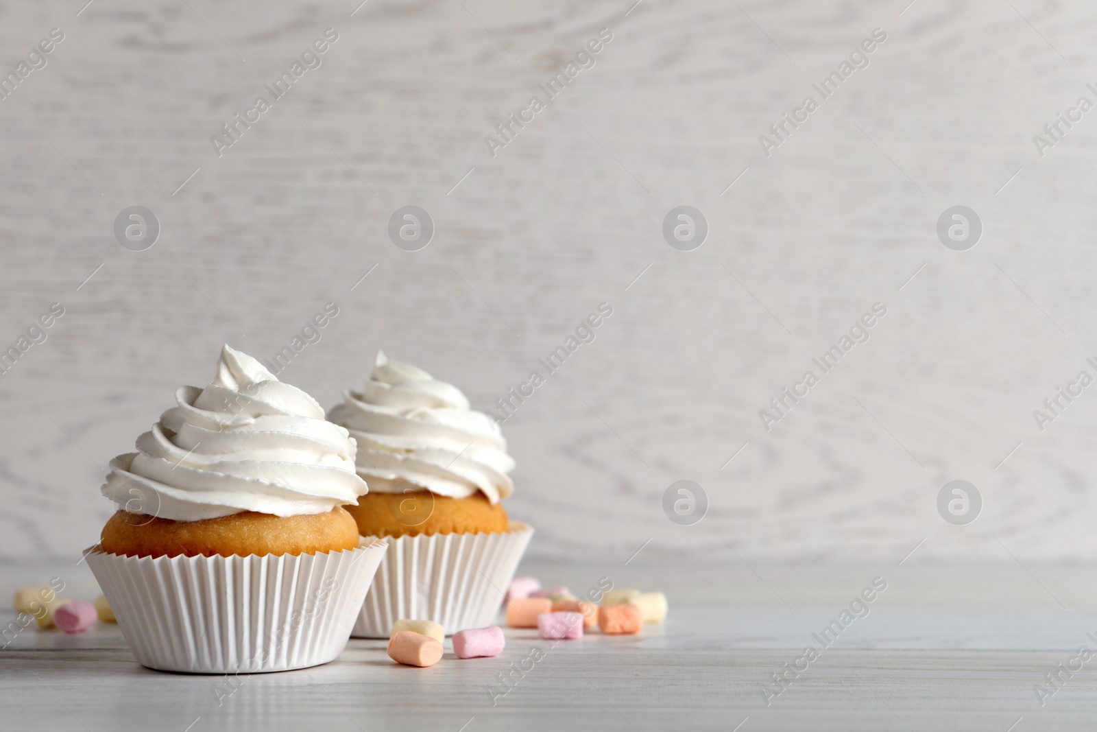 Photo of Delicious cupcakes with cream and marshmallows on white wooden table. Space for text