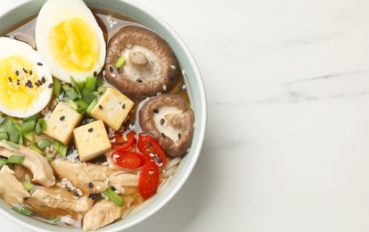 Photo of Bowl of delicious ramen on white marble table, top view with space for text. Noodle soup