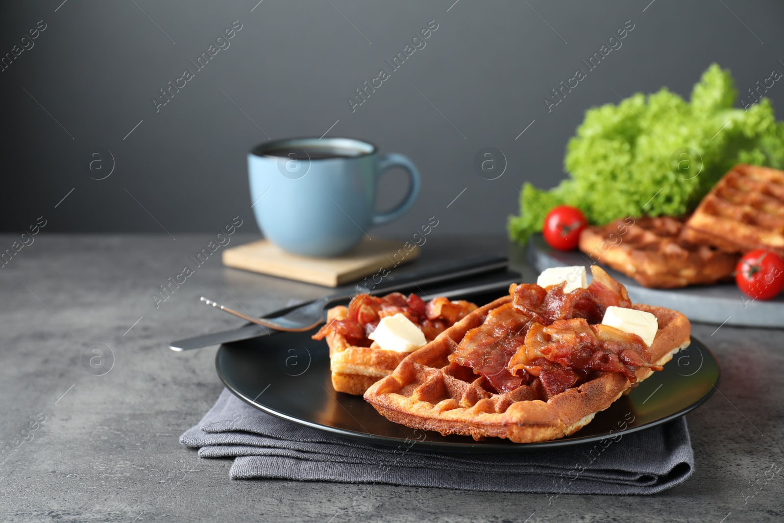 Photo of Tasty Belgian waffles served with bacon, butter and coffee on grey table. Space for text