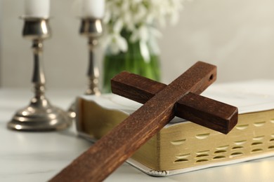 Wooden cross and Bible on white table, closeup