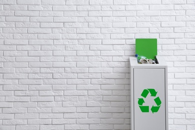 Photo of Overfilled trash bin with recycling symbol near brick wall. Space for text