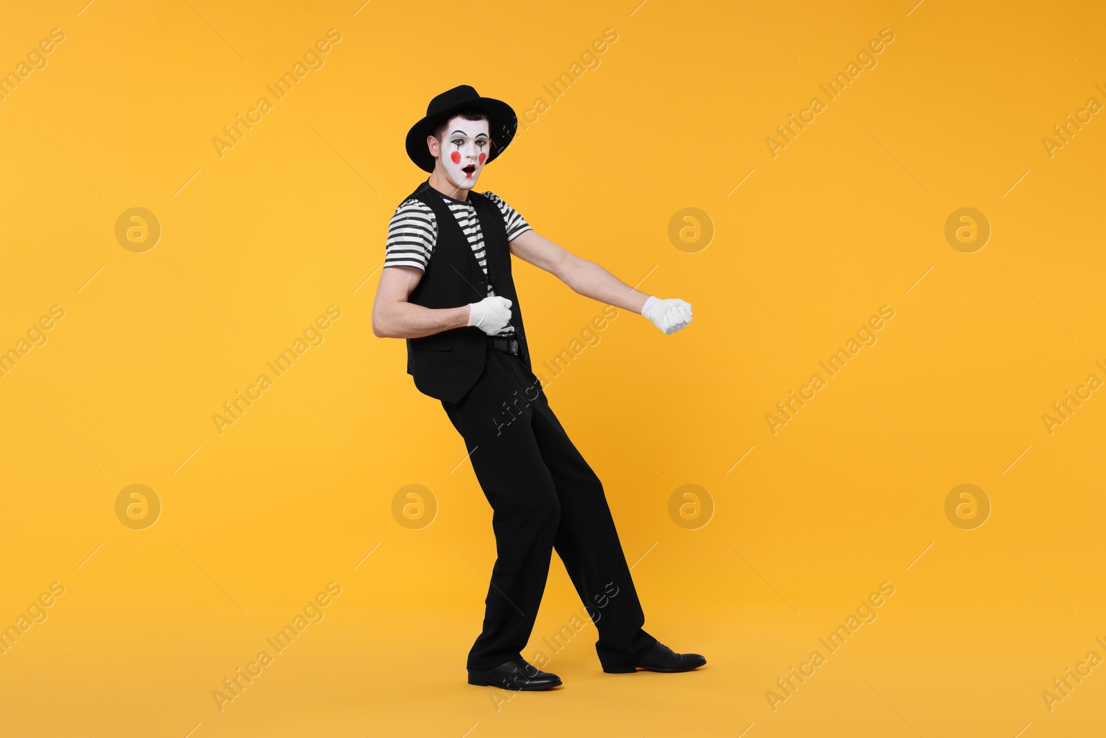 Photo of Funny mime artist in hat posing on orange background