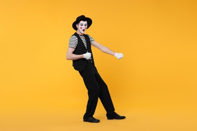 Photo of Funny mime artist in hat posing on orange background