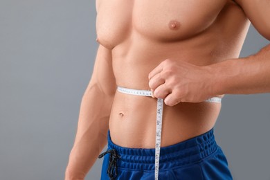 Photo of Athletic man measuring waist with tape on grey background, closeup. Weight loss concept