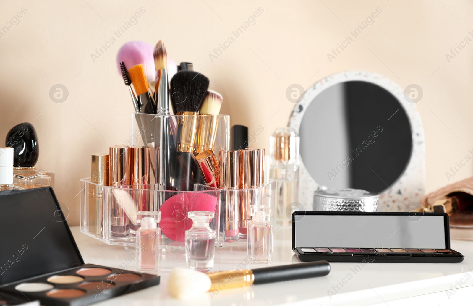 Photo of Luxury makeup products and accessories on dressing table with mirror near wall