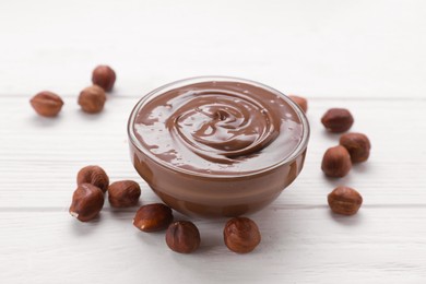 Photo of Bowl with delicious chocolate paste and nuts on white wooden table