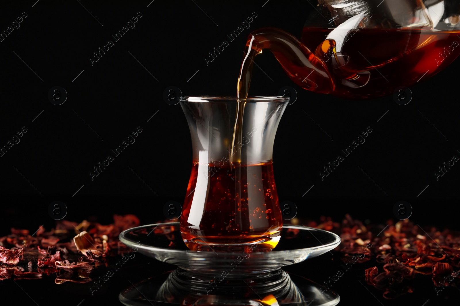 Photo of Pouring traditional Turkish tea from pot into glass on black table