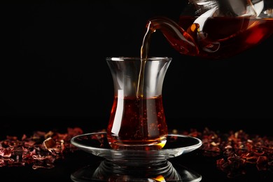 Photo of Pouring traditional Turkish tea from pot into glass on black table