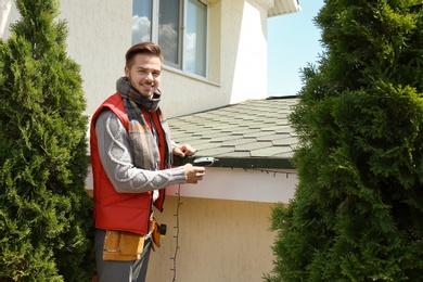 Young man decorating roof with Christmas lights