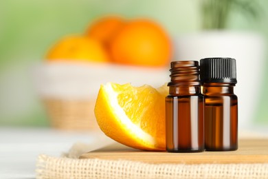 Photo of Bottles of essential oil and orange slice on wooden board, closeup