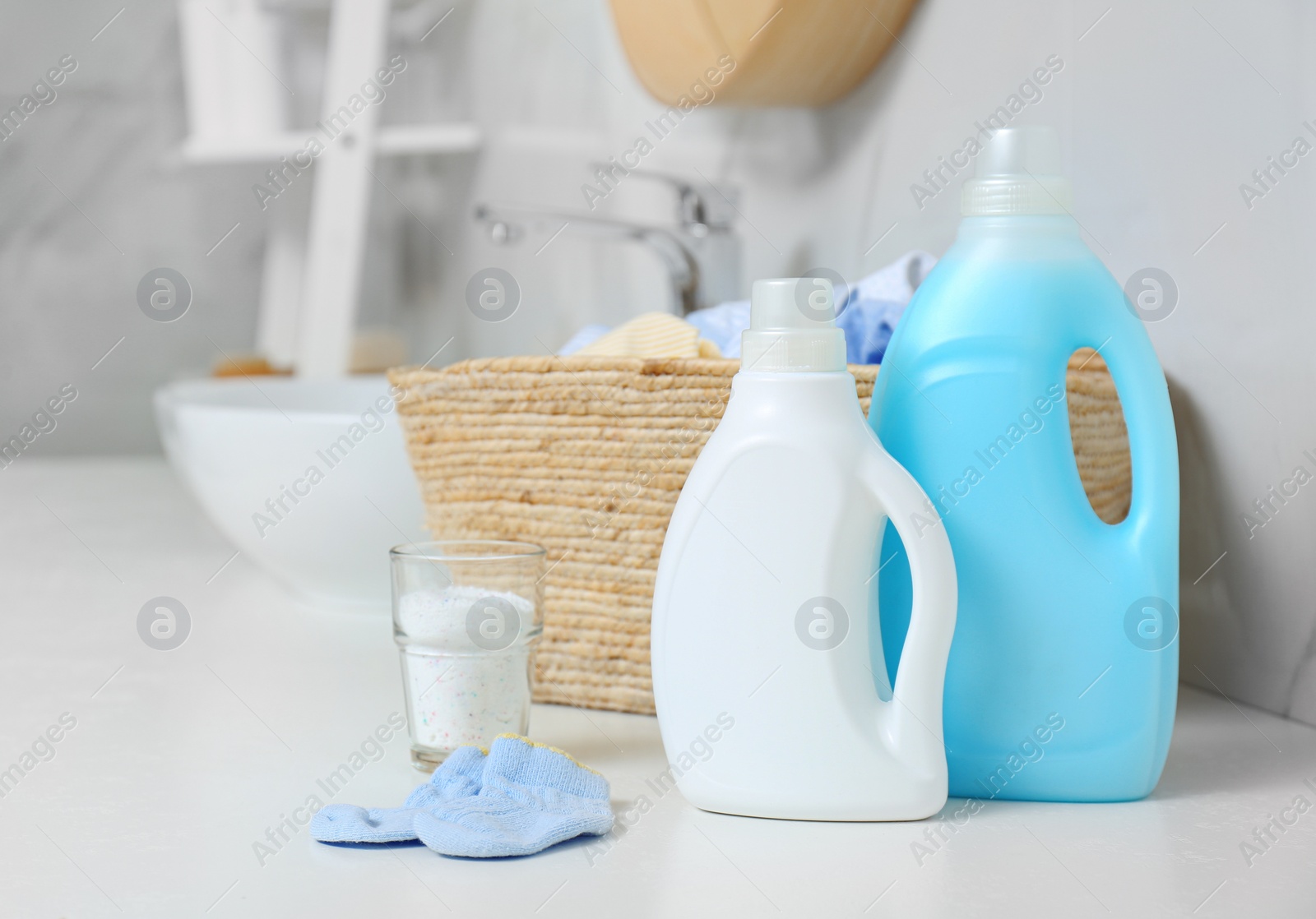 Photo of Bottles of detergent and children's clothes on countertop in bathroom