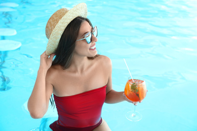 Woman with glass of refreshing drink in swimming pool