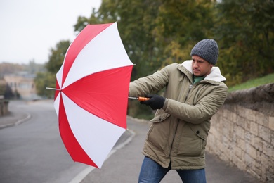 Photo of Man with colorful umbrella caught in gust of wind on street