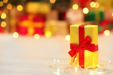 Photo of Beautifully wrapped gift box and festive lights on wooden table indoors, space for text. Christmas celebration