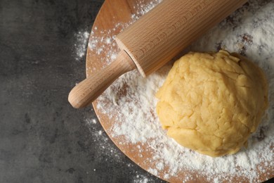 Making shortcrust pastry. Raw dough, flour and rolling pin on grey table, top view. Space for text