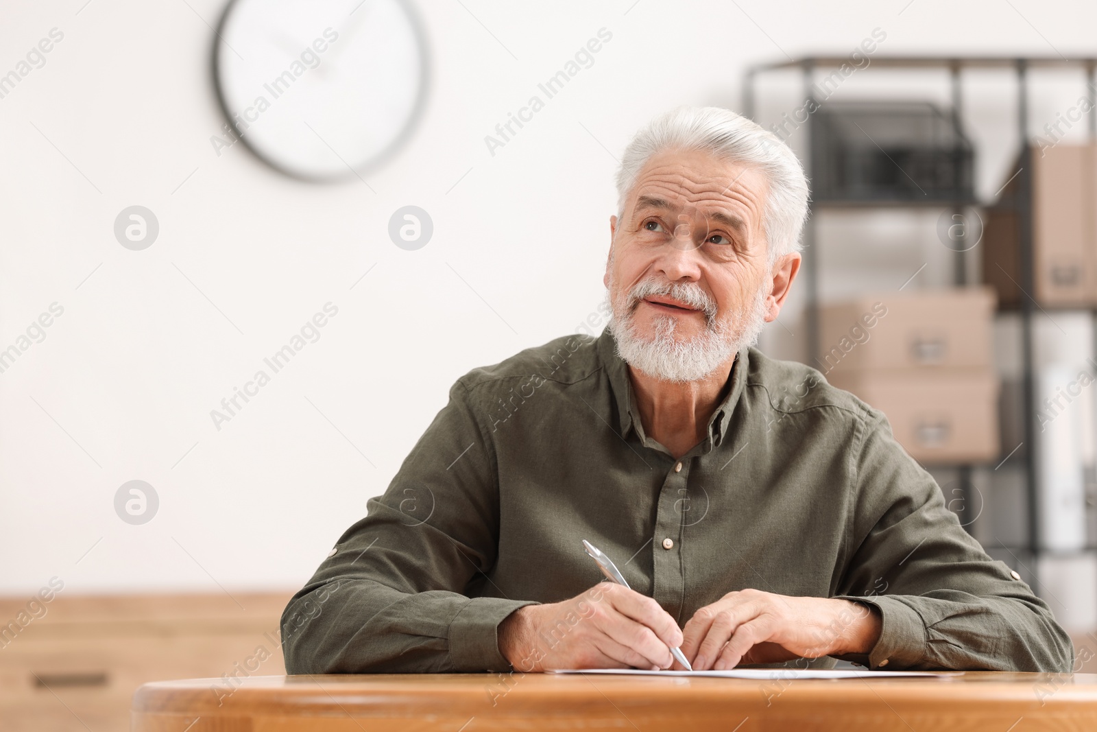 Photo of Senior man signing Last Will and Testament at table indoors. Space for text