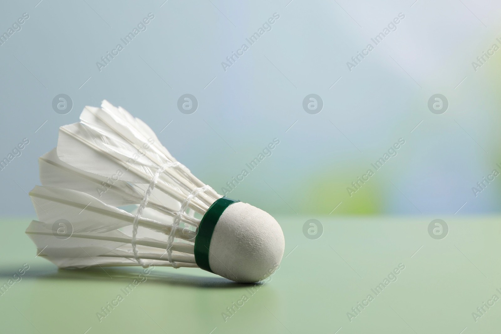 Photo of Feather badminton shuttlecock on green table against blurred background, closeup. Space for text