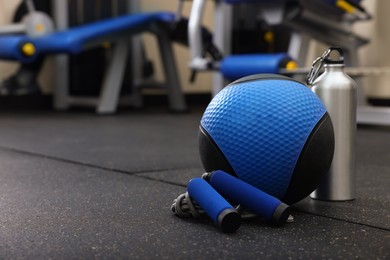 Photo of Blue medicine ball, bottle and skipping rope on floor in gym, space for text