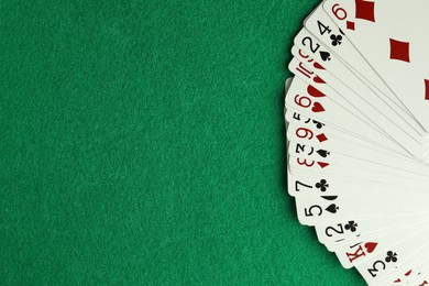 Photo of Fan of playing cards on green table, top view. Space for text