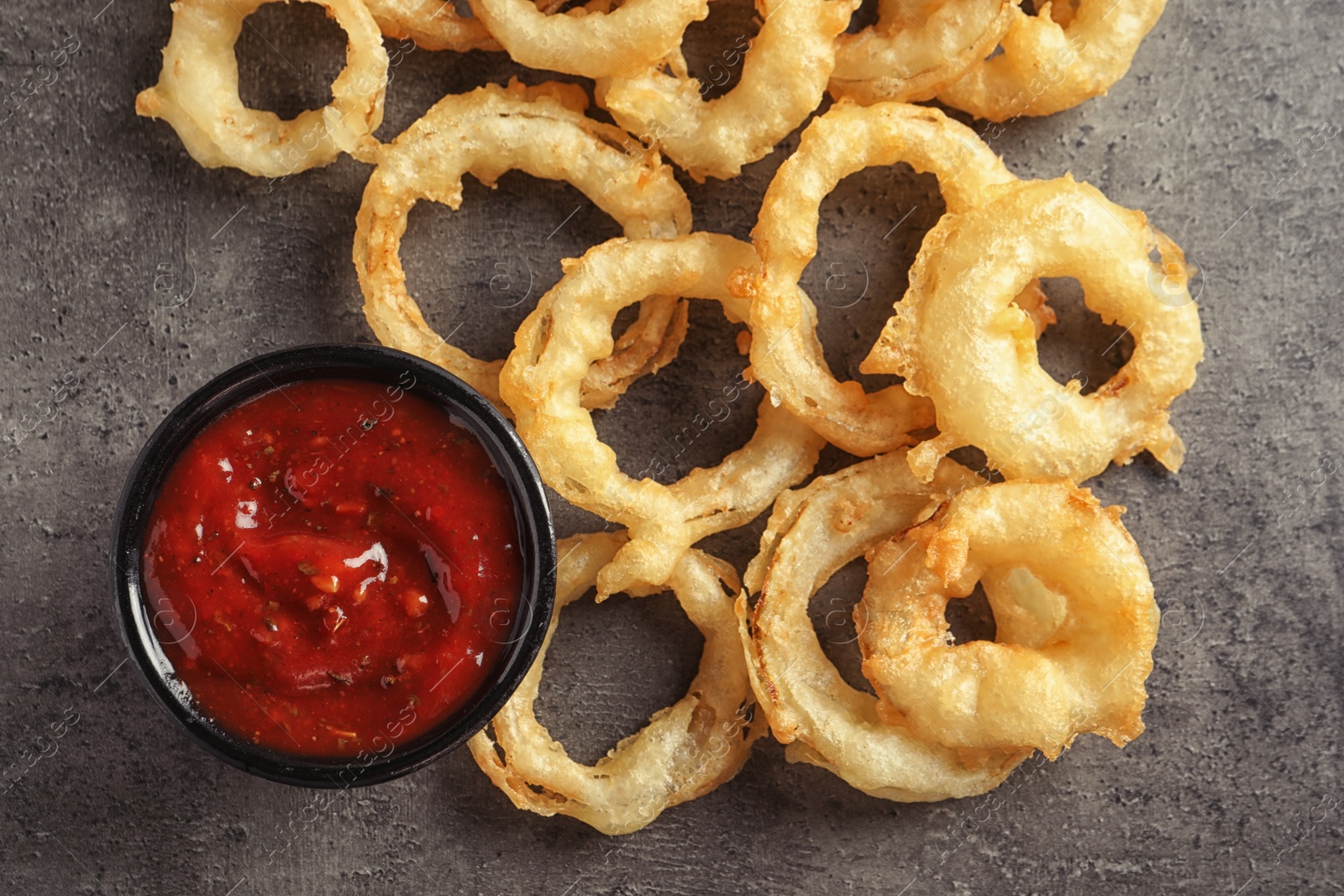 Photo of Delicious golden crispy onion rings and sauce on gray background, top view