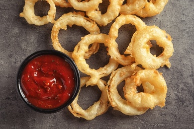 Photo of Delicious golden crispy onion rings and sauce on gray background, top view
