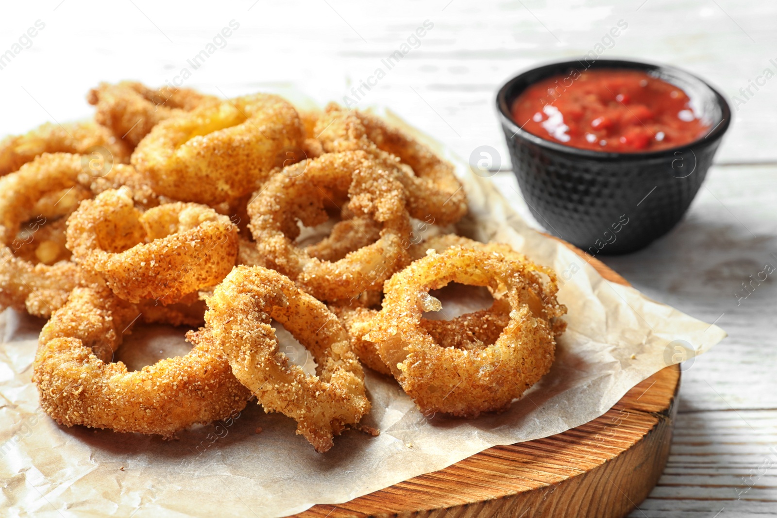 Photo of Homemade crunchy fried onion rings with tomato sauce on wooden table, closeup