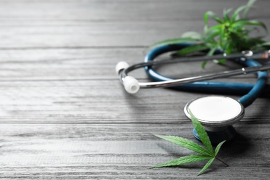 Photo of Hemp leaves and stethoscope on grey wooden table. Space for text