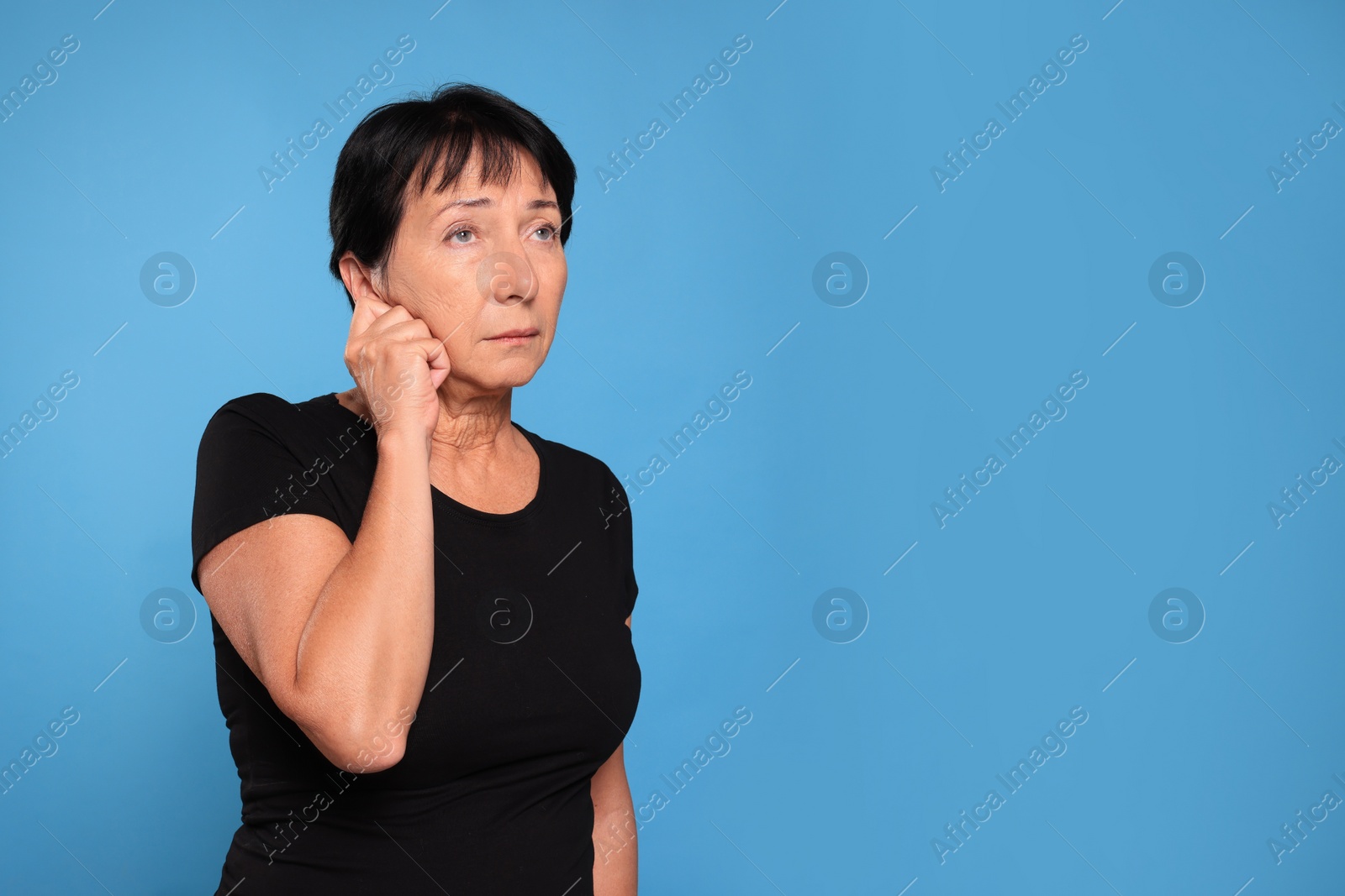 Photo of Senior woman suffering from ear pain on light blue background. Space for text