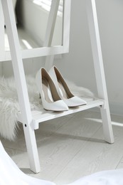Pair of white wedding high heel shoes on wooden rack indoors