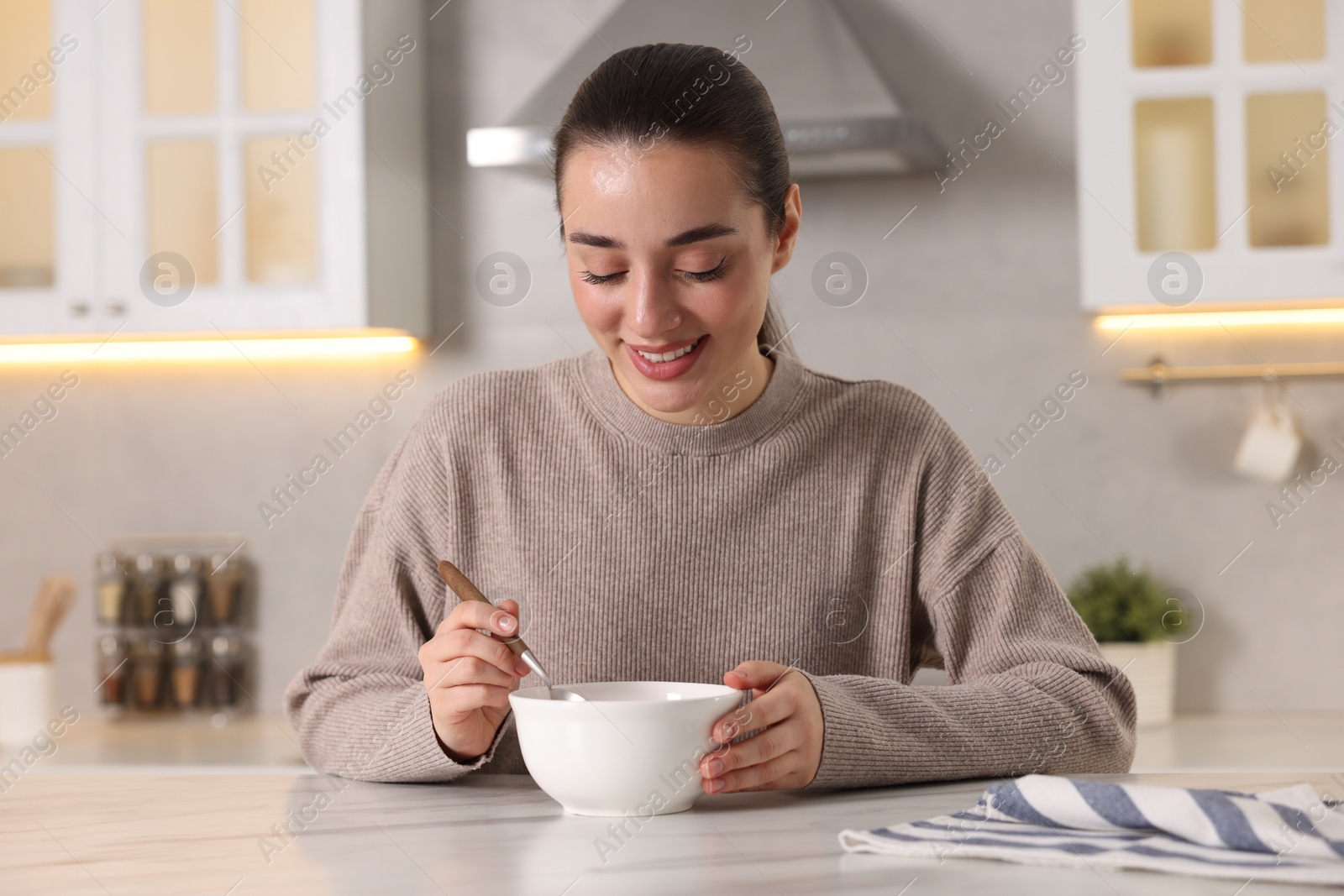 Photo of Smiling woman eating tasty soup at white marble table in kitchen