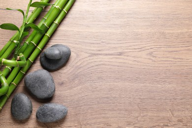 Photo of Spa stones and bamboo stems on wooden table, flat lay. Space for text