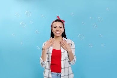 Young woman having fun with soap bubbles on light blue background