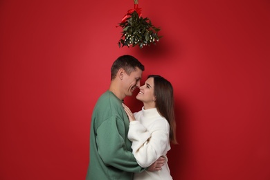 Happy couple standing under mistletoe bunch on red background