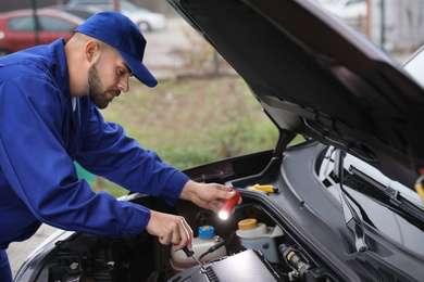 Photo of Young mechanic with flashlight fixing car outdoors