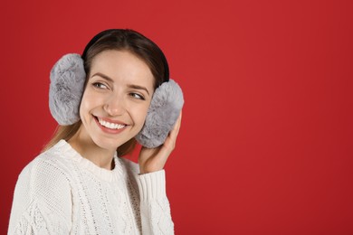 Happy woman wearing warm earmuffs on red background, space for text