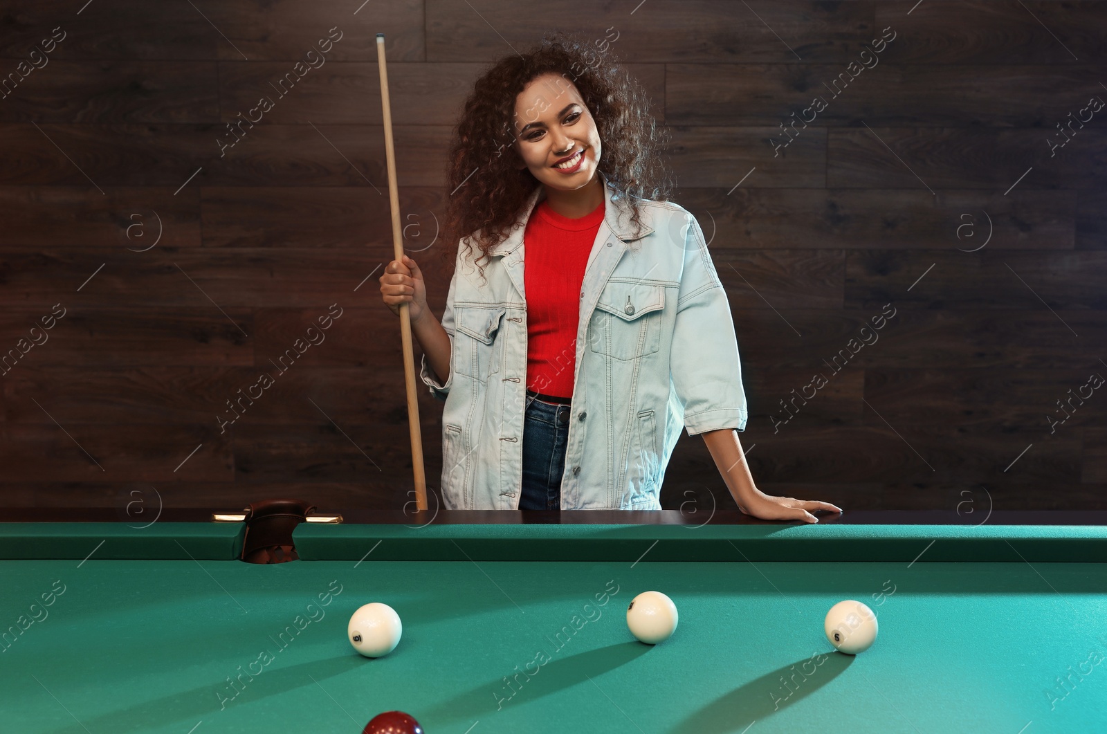 Photo of Young African-American woman with cue near billiard table indoors